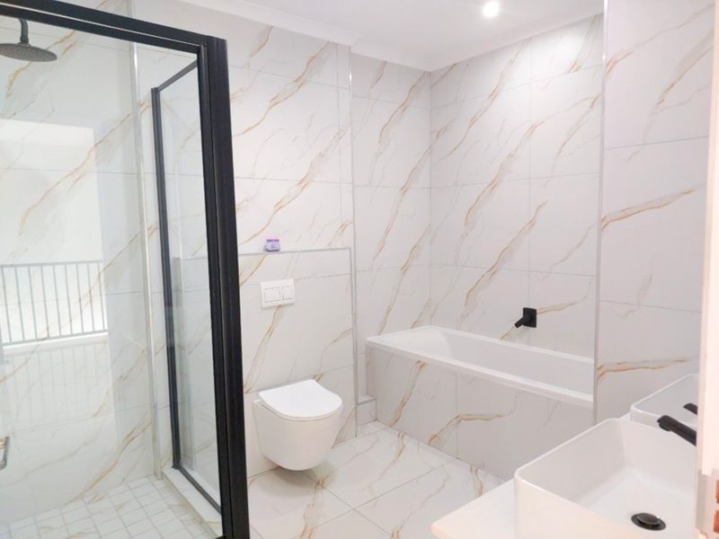 Modern bathroom featuring marble-look tiling, a walk-in shower with black frame, a wall-mounted toilet, and a built-in bathtub with contemporary black fixtures.
