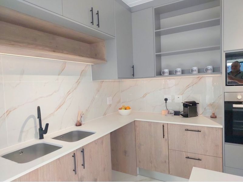 Modern kitchen featuring wood-grain cabinetry, marble-look splashback, quartz countertops, and integrated oven with sleek matte black fixtures.