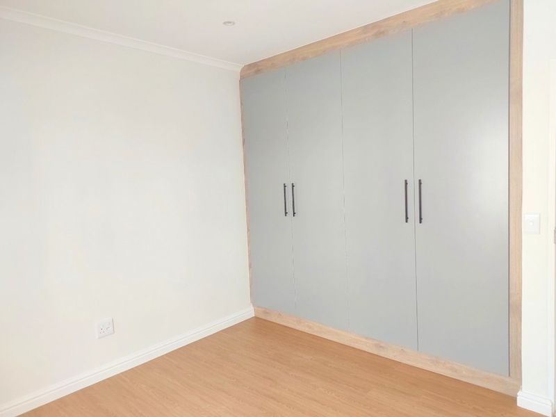 A clean, modern bedroom featuring light-toned laminate flooring and floor-to-ceiling built-in cupboards with a contemporary grey finish.
