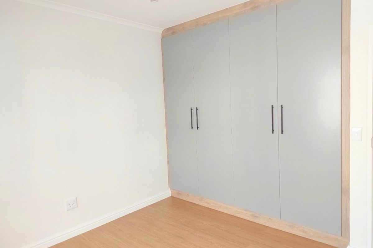 A clean, modern bedroom featuring light-toned laminate flooring and floor-to-ceiling built-in cupboards with a contemporary grey finish.