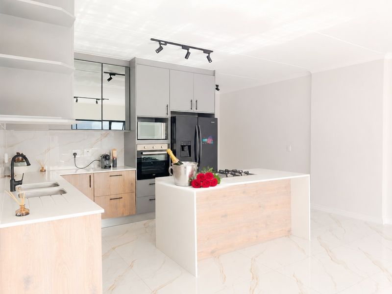 Modern kitchen featuring light wood and grey cabinetry, stone countertops, a central island with a gas hob, and high-end built-in appliances.