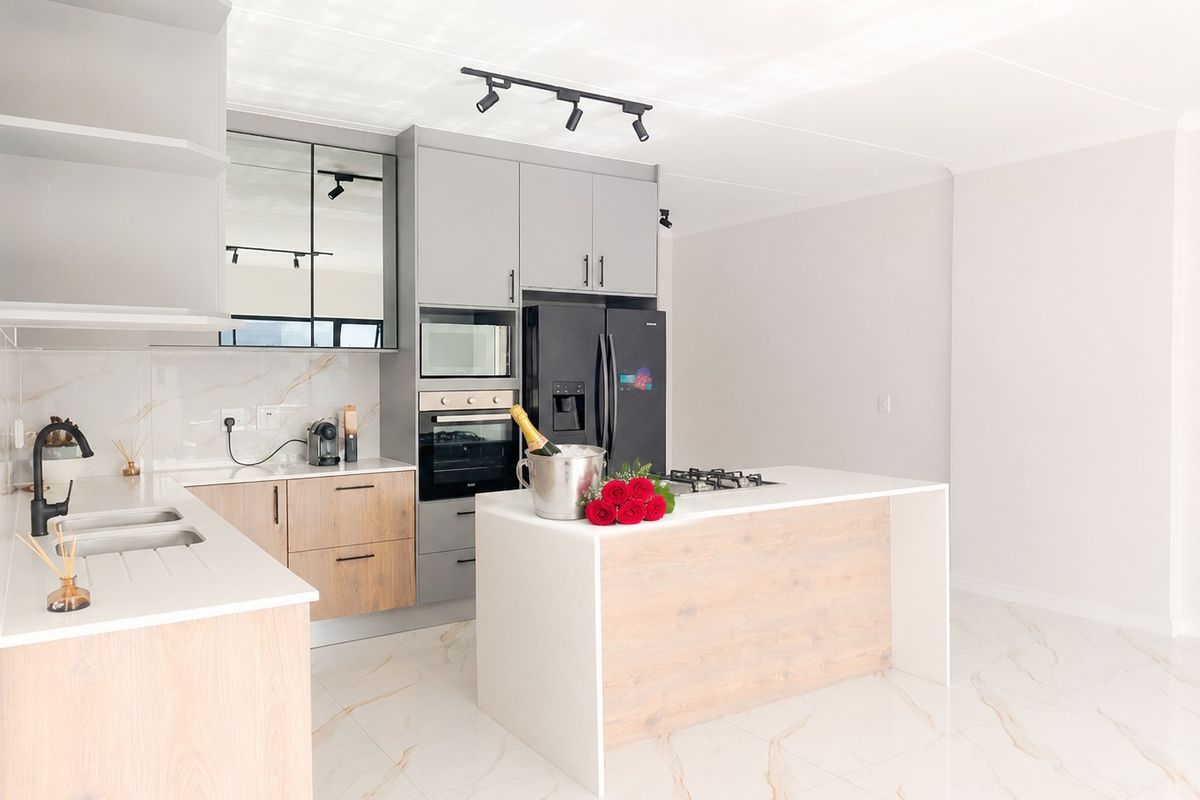 Modern kitchen featuring light wood and grey cabinetry, stone countertops, a central island with a gas hob, and high-end built-in appliances.