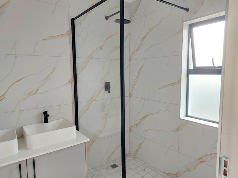 Modern bathroom featuring a walk-in shower with black frame, dual countertop basins on a vanity cabinet, and elegant marble-look wall tiling.