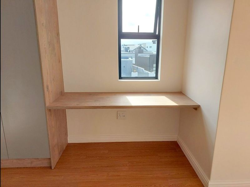 A clean, modern home office space featuring a built-in wooden desk, integrated cabinetry, and laminate flooring with a window view.