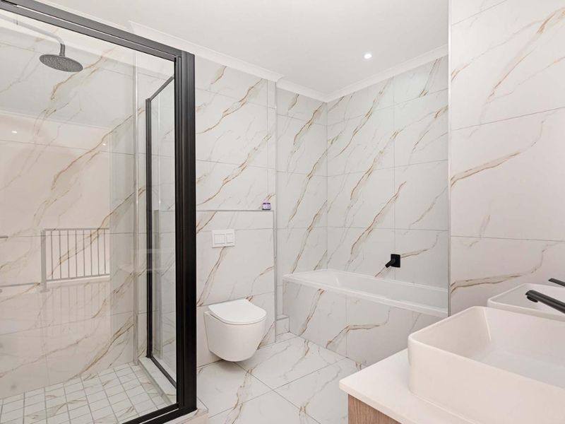 Modern bathroom featuring a walk-in shower, wall-hung toilet, built-in bathtub, and double vanity with contemporary black matte fixtures and elegant marble-look tiling.