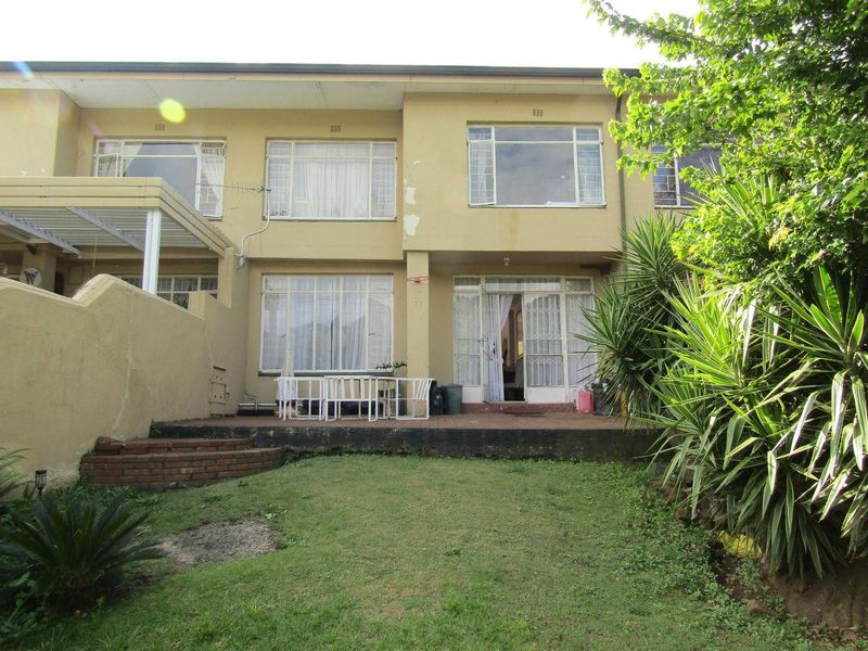 Rear view of the apartment building featuring a brick patio, sliding glass doors, and a small private garden area.