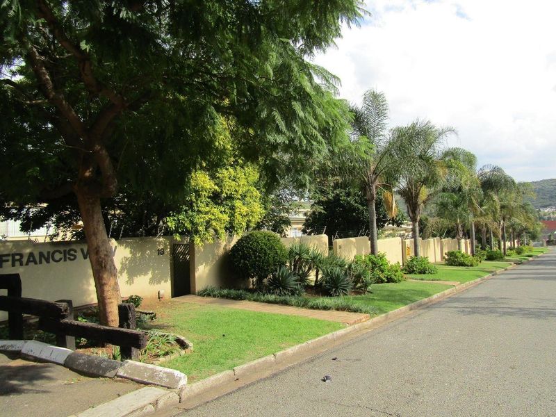 Street view of the property complex entrance featuring a well-maintained boundary wall, mature trees, and landscaped verge.