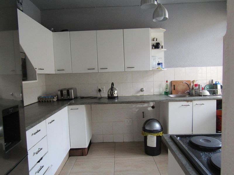 A functional kitchen featuring white cabinetry, laminate countertops, tiled backsplash, and a built-in electric hob with ceramic floor tiles.
