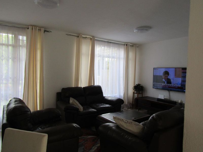 A living room featuring large windows with security gates and curtain rods, providing natural light to the space.