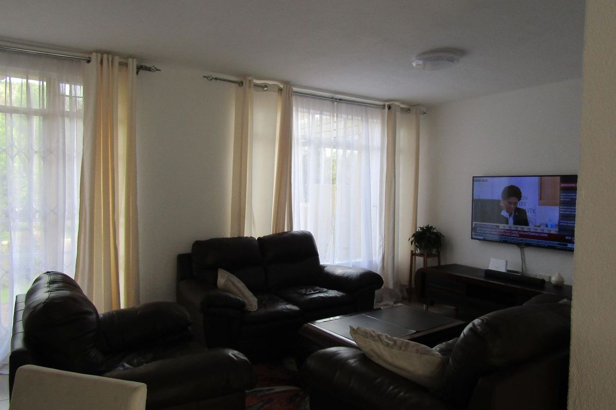 A comfortable living room featuring large windows with curtain rails and a wall-mounted television, providing a functional and well-lit space.