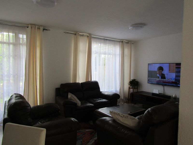 A comfortable living room featuring large windows with curtain rails and a wall-mounted television, providing a functional and well-lit space.