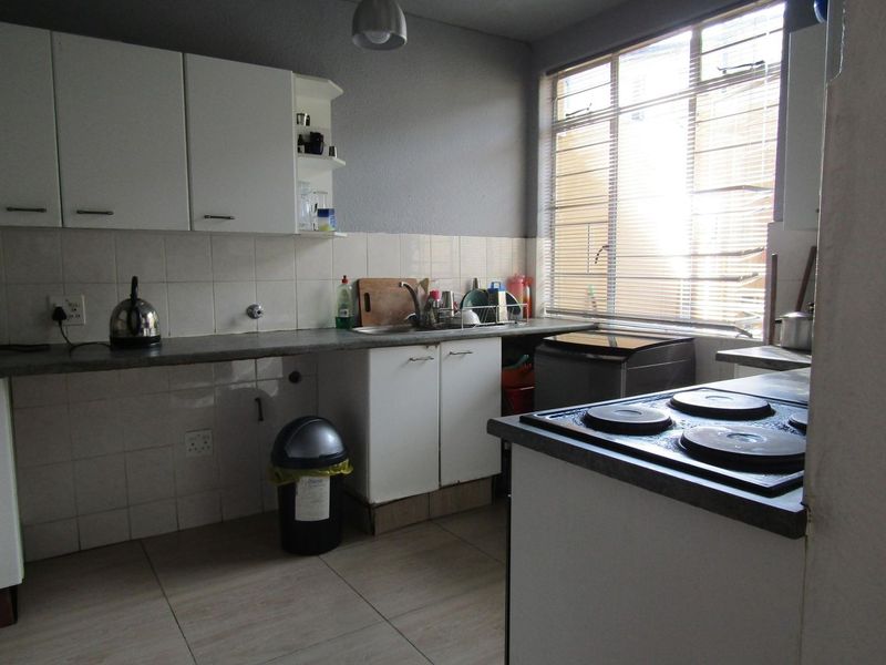 Functional kitchen featuring built-in cabinetry, laminate countertops, a stainless steel sink, and an electric hob with tiled splashback and flooring.