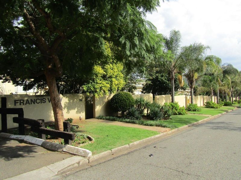 Street view of the property boundary wall, featuring established landscaping, pedestrian access, and secure perimeter fencing along the road frontage.