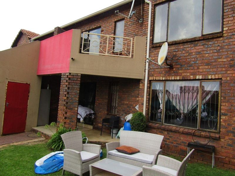 Rear view of a double-story brick apartment featuring a balcony with metal balustrade, ground-level tiled patio, and security bars on windows.