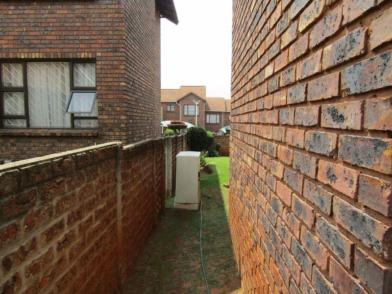 A narrow side passage between two face brick apartment buildings, featuring a small lawn area and boundary wall.