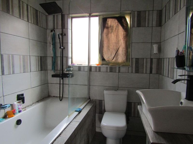 A compact bathroom featuring a bathtub with a shower head, a vessel sink, and tiled walls. The space requires minor maintenance and cosmetic updates.