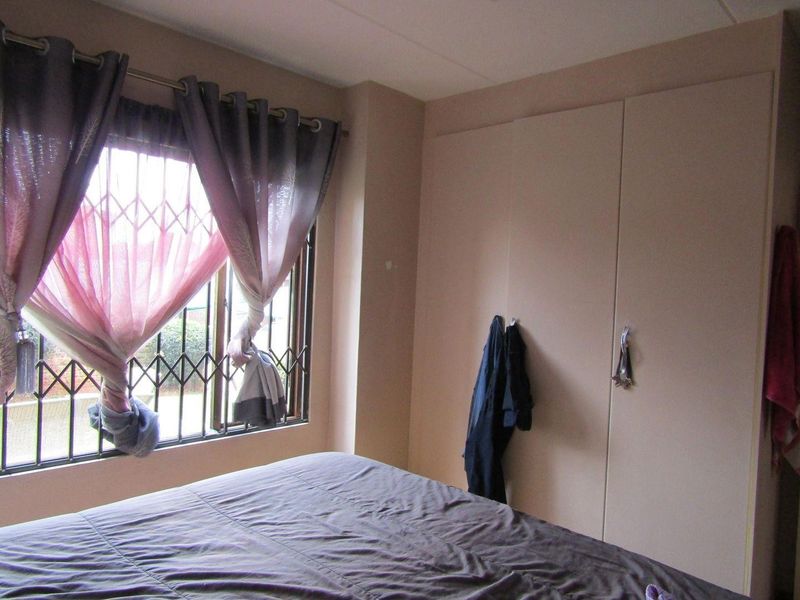 A bedroom featuring built-in cupboards and a window fitted with security burglar bars.