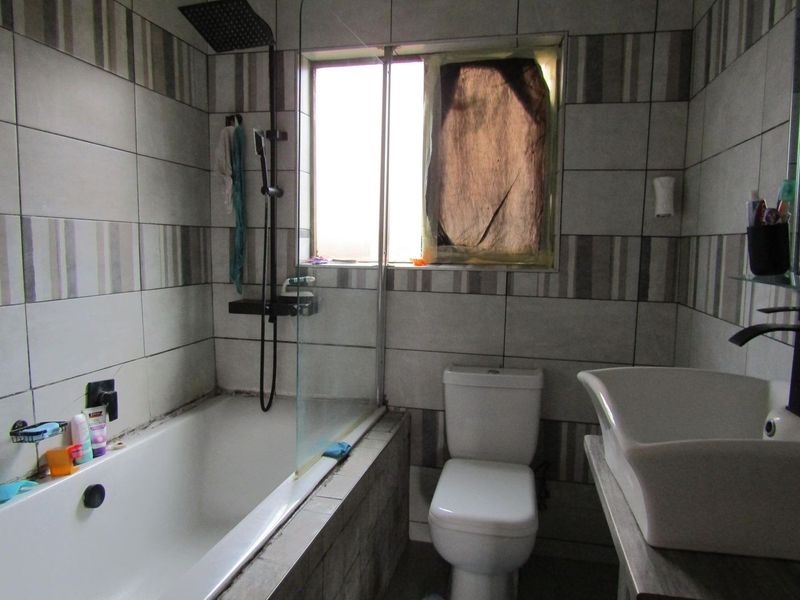 A functional bathroom featuring a built-in bathtub with a shower screen, a toilet, and a vessel sink with tiled wall finishes.
