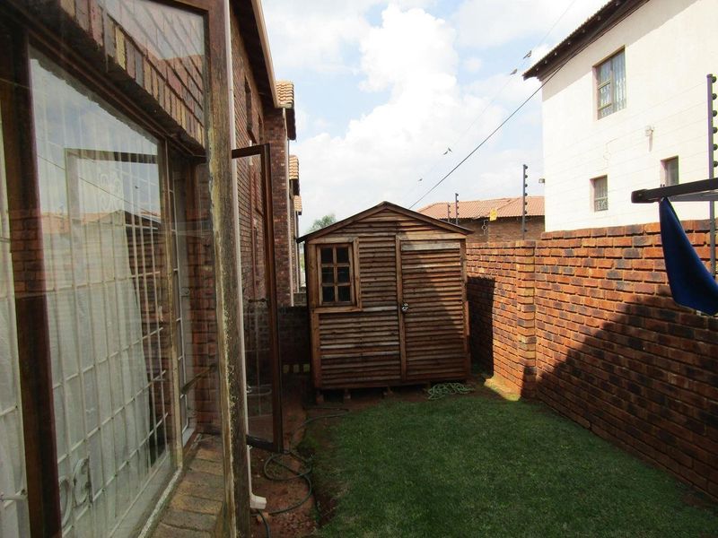 A rear exterior view of the property featuring a small lawn, a wooden garden shed, and a brick boundary wall with electric fencing.