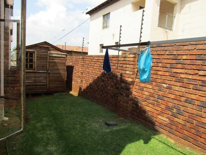 A private rear garden area featuring a brick boundary wall with electric fencing, a small wooden storage shed, and a lawn.