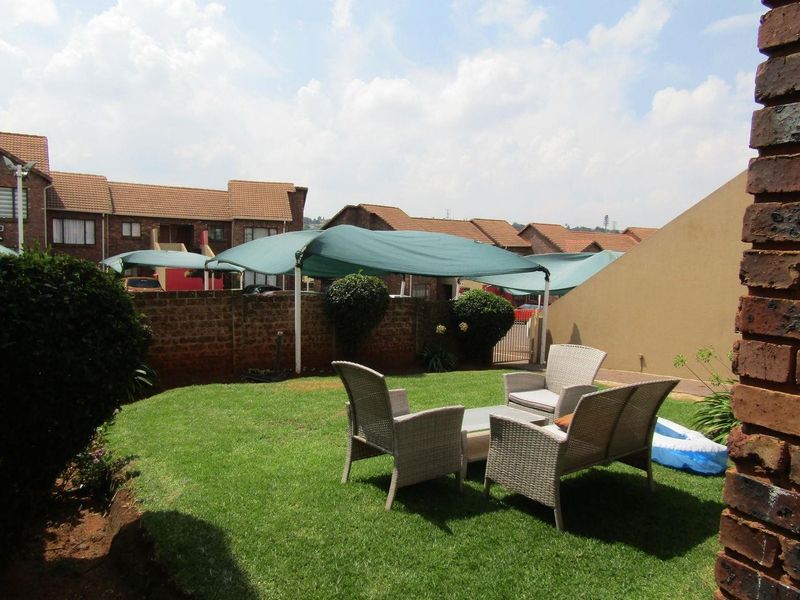 A private rear garden area featuring a well-maintained lawn, brick boundary wall, and a shade sail structure for outdoor comfort.