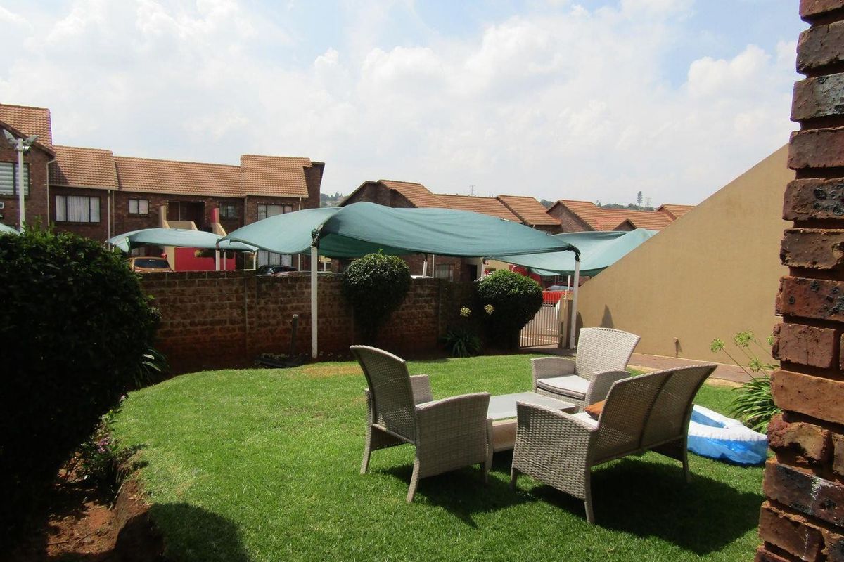 A private rear garden area featuring a well-maintained lawn, brick boundary wall, and a shade sail structure for outdoor comfort.