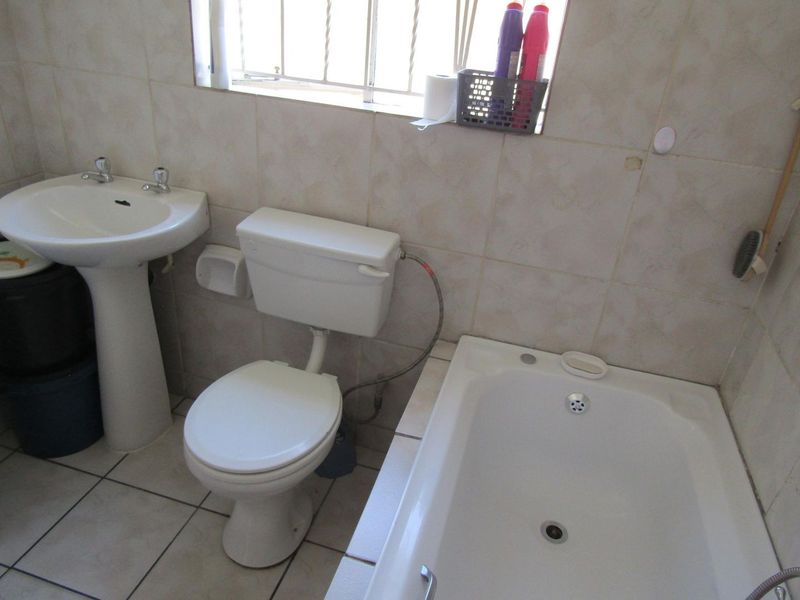 A functional bathroom featuring a pedestal washbasin, standard toilet, and built-in bathtub with neutral ceramic wall and floor tiling.