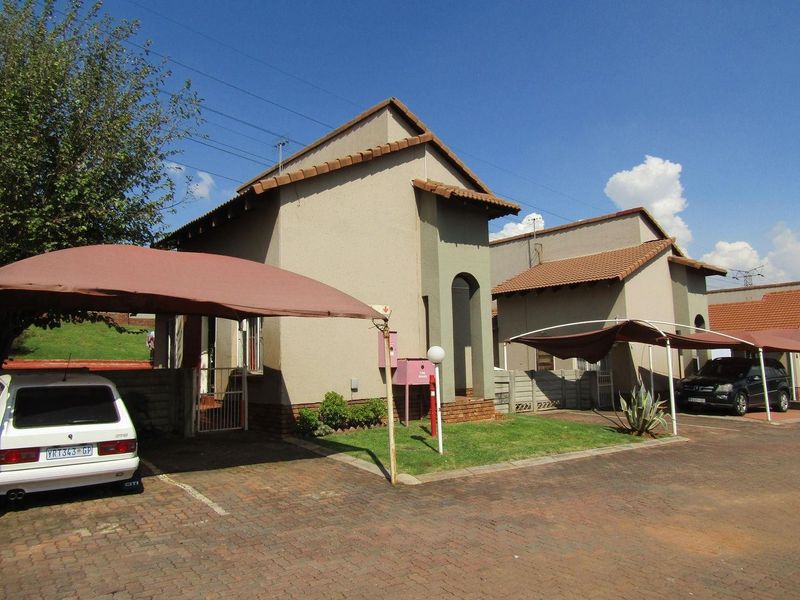 Front exterior view of a townhouse complex featuring paved driveways, covered carports, and tiled roof structures.