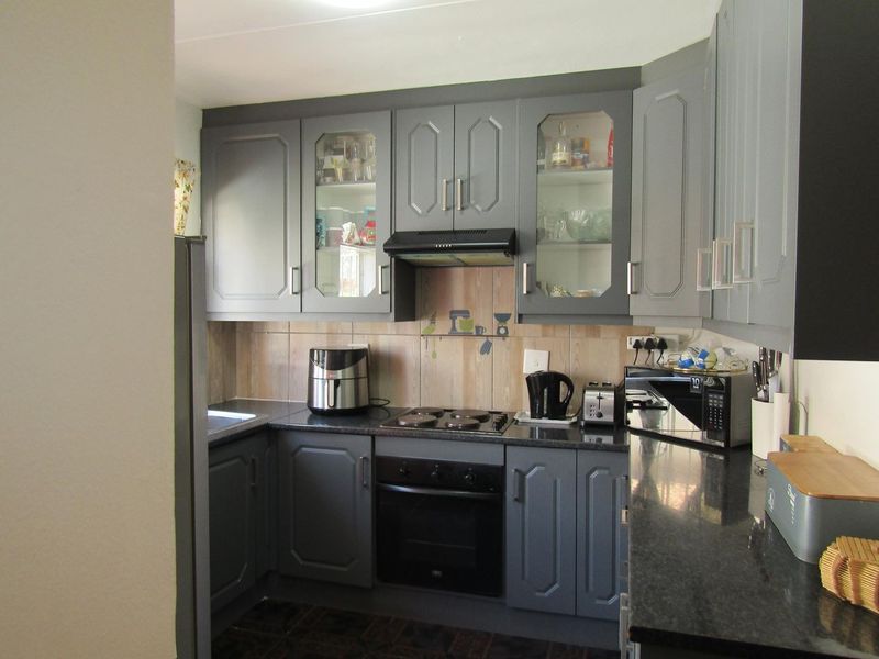A functional kitchen featuring grey cabinetry, granite countertops, a built-in oven, electric hob, and a tiled backsplash.