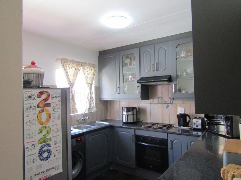 A functional kitchen featuring grey cabinetry, granite countertops, a double sink, and built-in cooking appliances with a tiled backsplash.