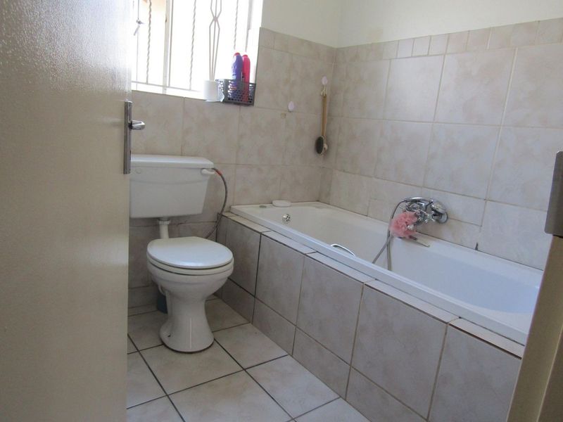 A functional bathroom featuring a built-in bathtub, standard toilet, and neutral ceramic tiling throughout.