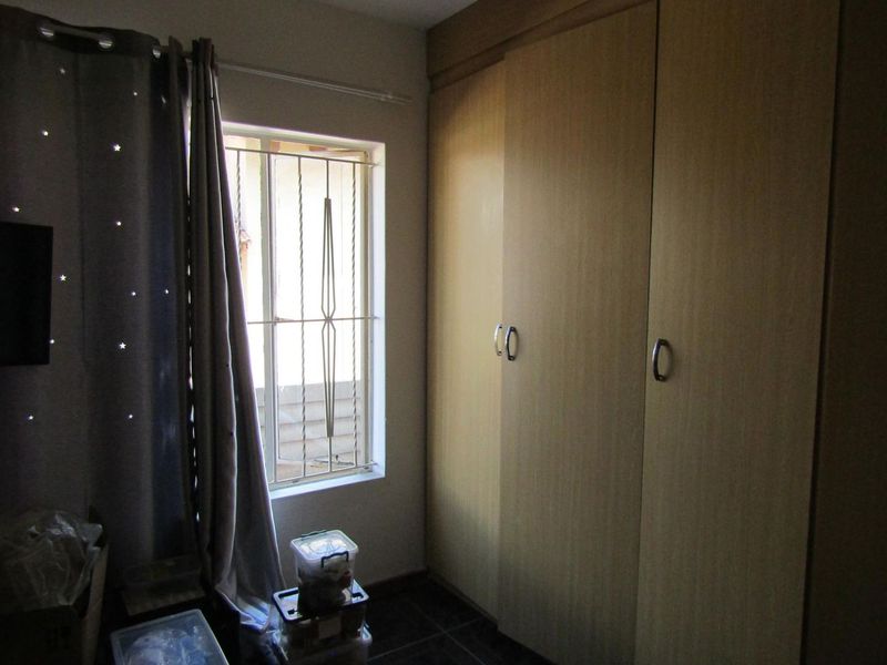 A bedroom featuring built-in cupboards, tiled flooring, and a window fitted with security bars.