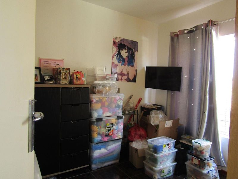 A bedroom space featuring a wall-mounted television and neutral wall finishes, currently utilized for storage.