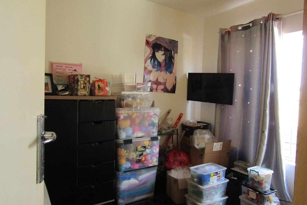 A bedroom space featuring a wall-mounted television and neutral wall finishes, currently utilized for storage.