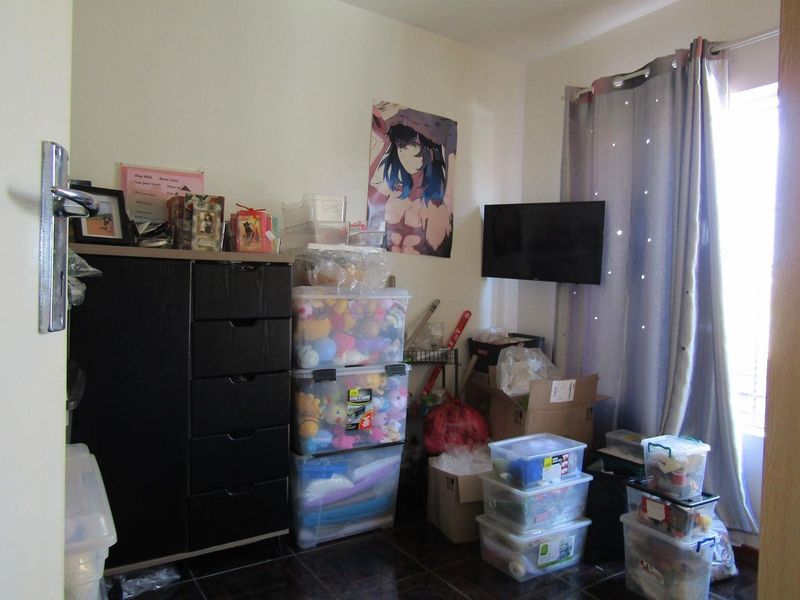A bedroom featuring tiled flooring and a window with curtain rails, currently utilized for storage.