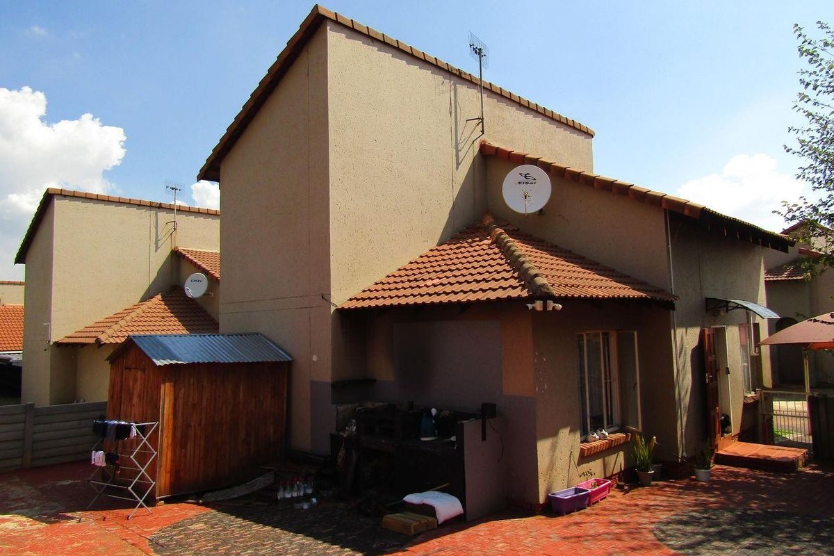 Rear exterior view of the townhouse featuring a brick-paved courtyard, built-in braai area, and terracotta tiled roofing.