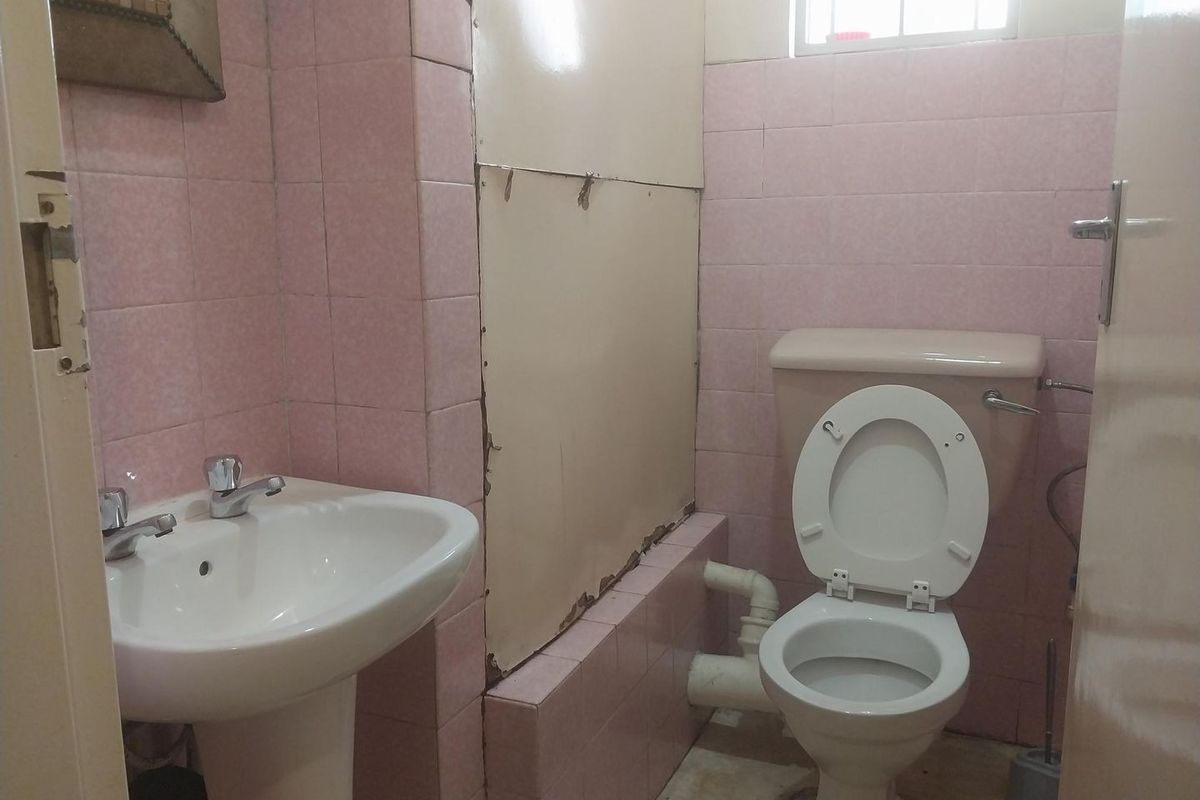 A dated bathroom featuring a pedestal basin and toilet with pink wall tiles and visible plumbing, requiring renovation to modernize the space.