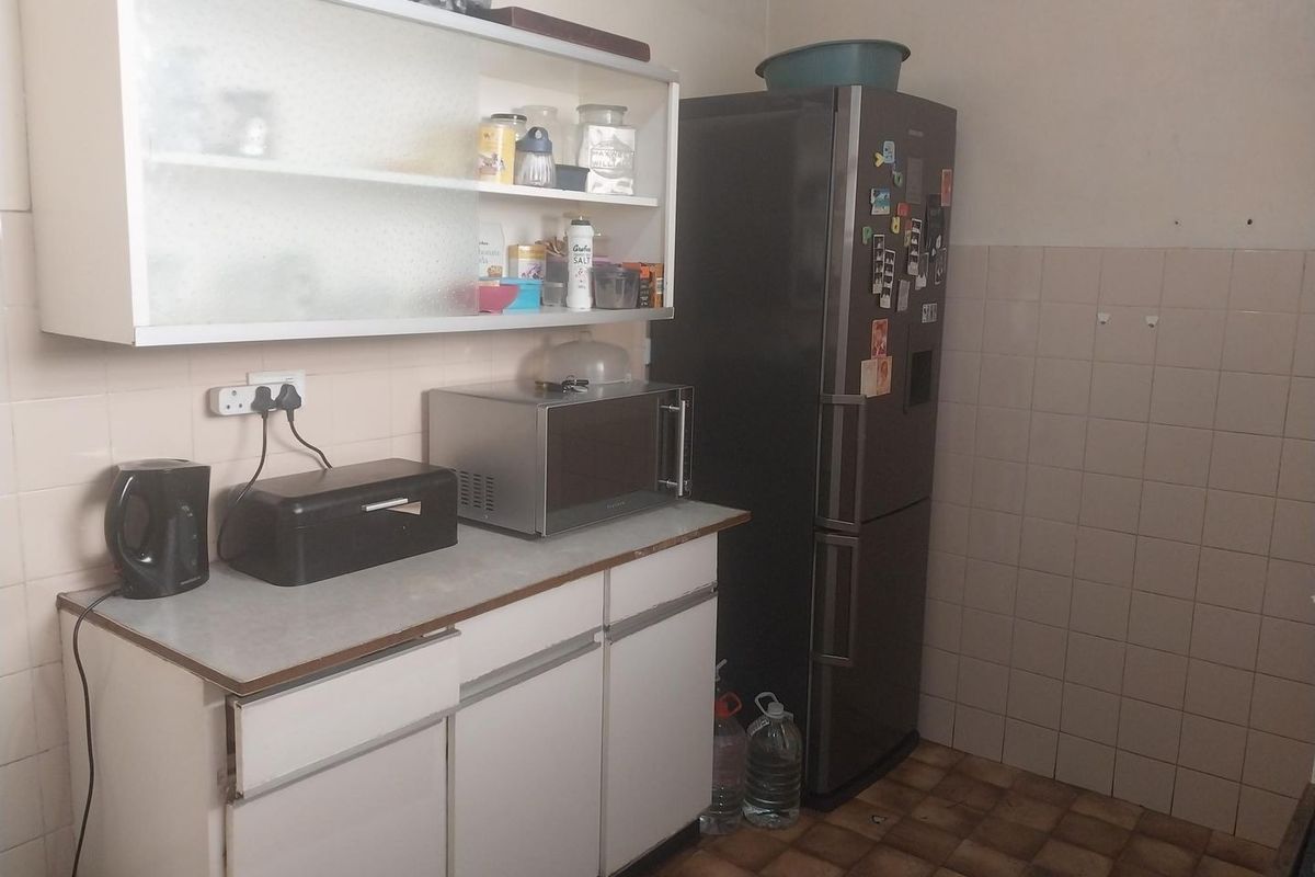 A functional kitchen area featuring white base and wall-mounted cabinetry, tiled splashbacks, and laminate countertops, offering potential for modernization.