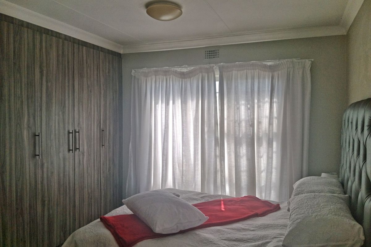 A well-maintained bedroom featuring floor-to-ceiling built-in cupboards with a modern wood-grain finish and classic ceiling cornice detailing.