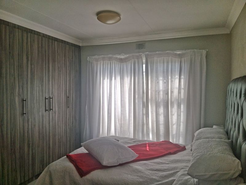 A well-maintained bedroom featuring floor-to-ceiling built-in cupboards with a modern wood-grain finish and classic ceiling cornice detailing.