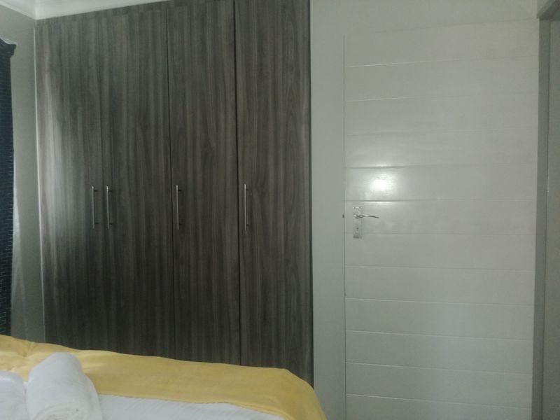 A bedroom featuring modern dark wood-grain built-in cupboards and a clean white interior door.