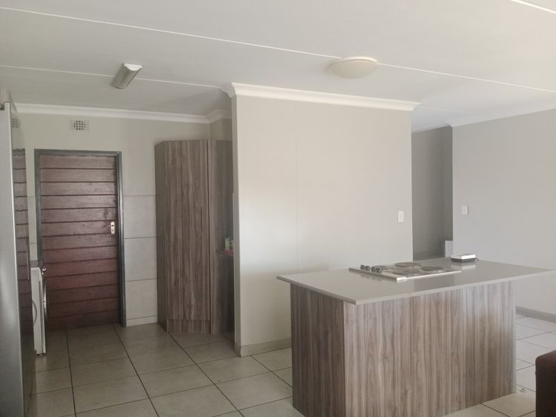A clean, modern kitchen area featuring a central island with a built-in hob, tiled flooring, and neutral cabinetry.
