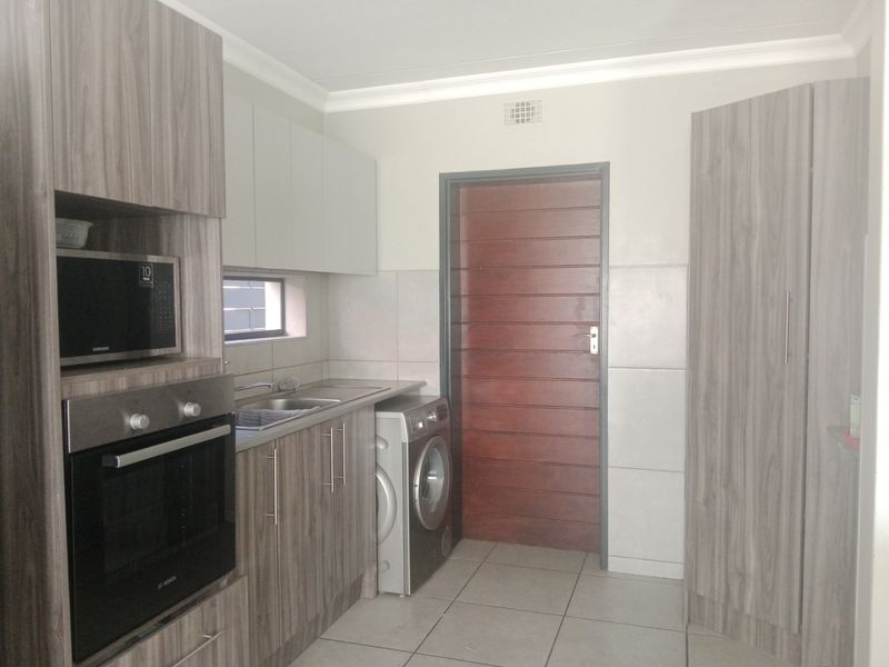 A functional laundry area featuring modern wood-grain cabinetry, built-in oven and microwave, stainless steel sink, and tiled flooring.