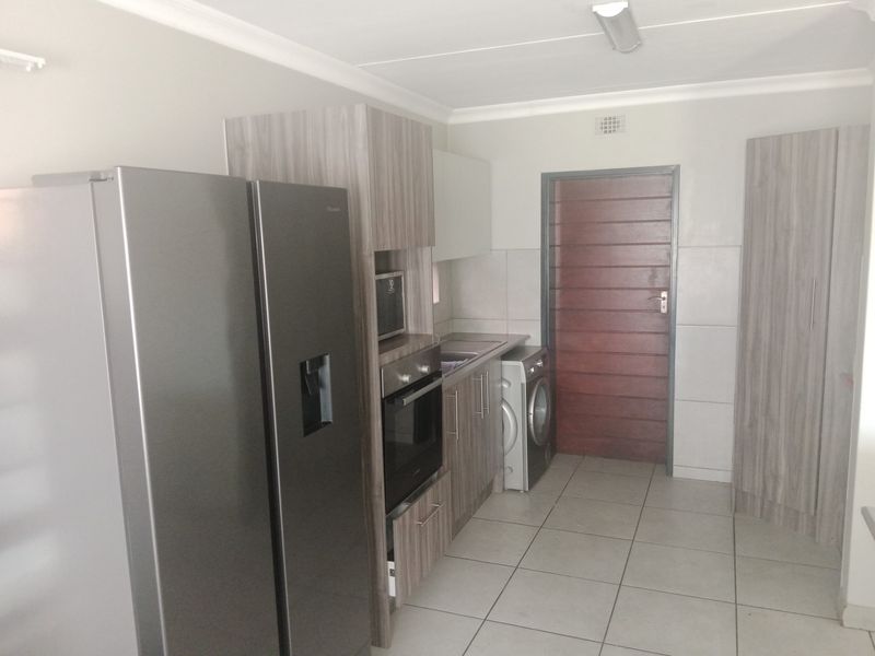 A functional kitchen featuring modern wood-look cabinetry, built-in oven, integrated microwave, and tiled flooring with direct access to an exterior door.
