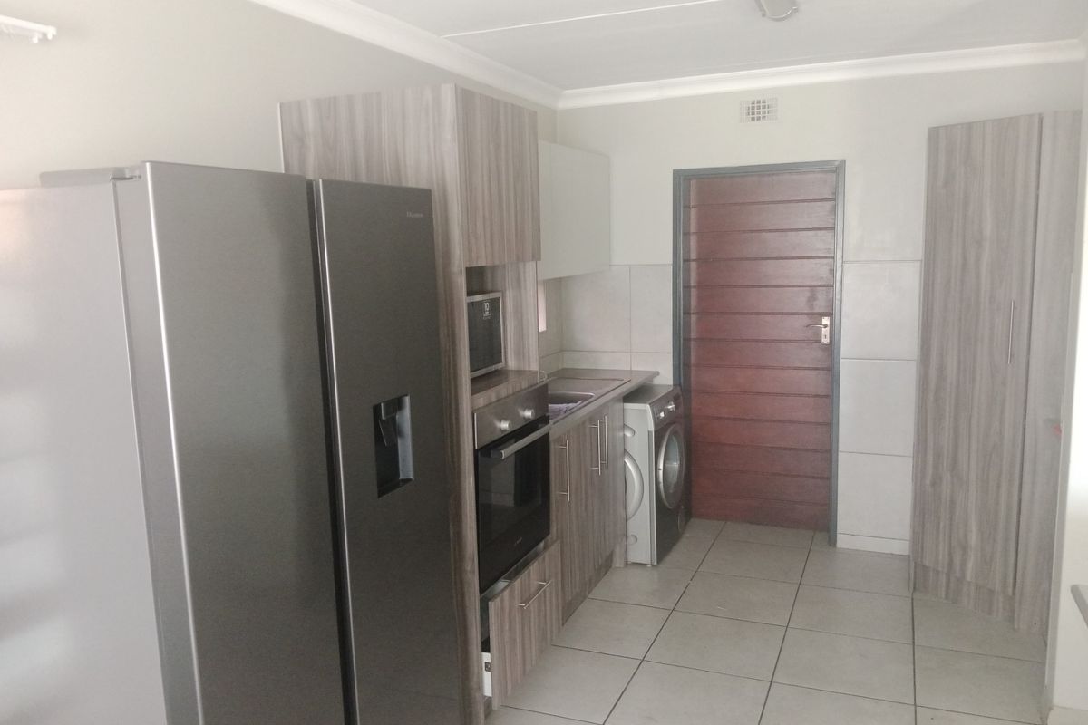 A functional kitchen featuring modern wood-look cabinetry, built-in oven, integrated microwave, and tiled flooring with direct access to an exterior door.