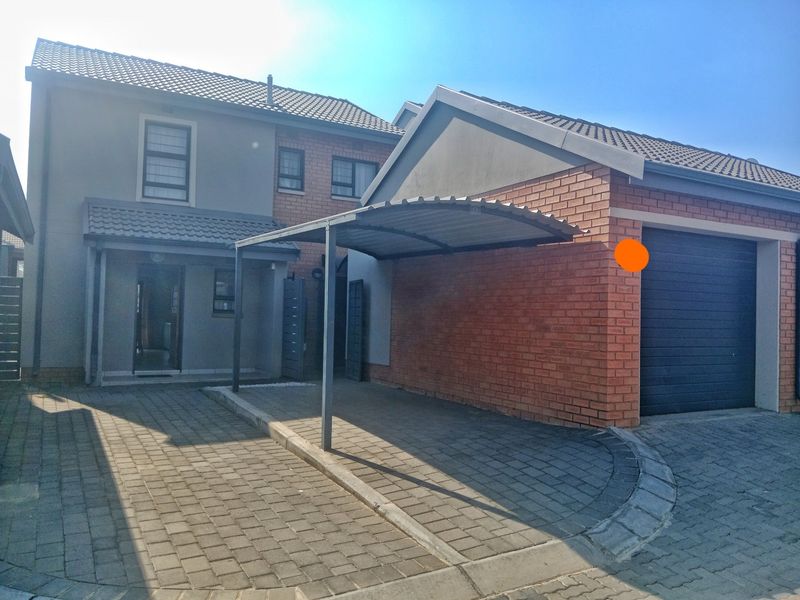 Front exterior view featuring a paved driveway, a covered carport, and a single garage with a brick and plastered facade.