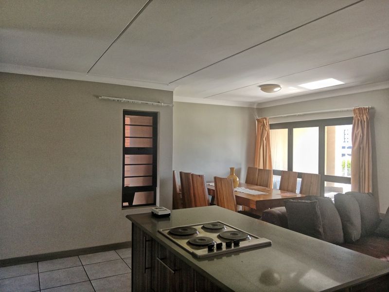 Open-plan living and dining area featuring a kitchen island with an integrated electric hob, tiled flooring, and large sliding doors leading to the exterior.