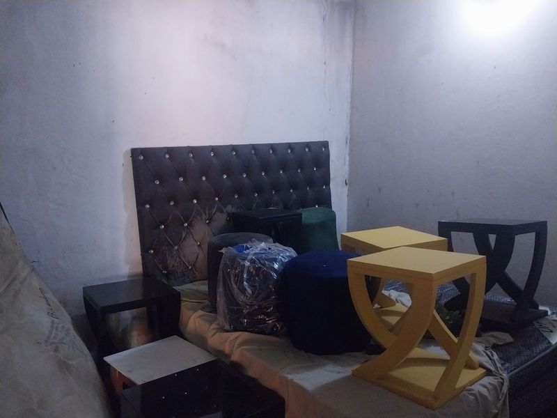 A bedroom space featuring a tufted headboard, currently cluttered with various furniture items and showing signs of wall wear.