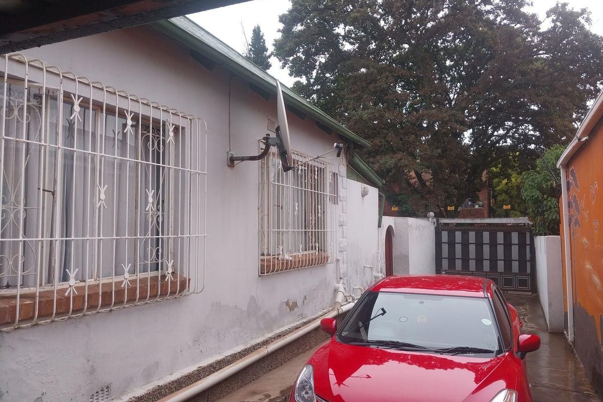 Side exterior view of the property showing a paved driveway, security bars on windows, and boundary walling.