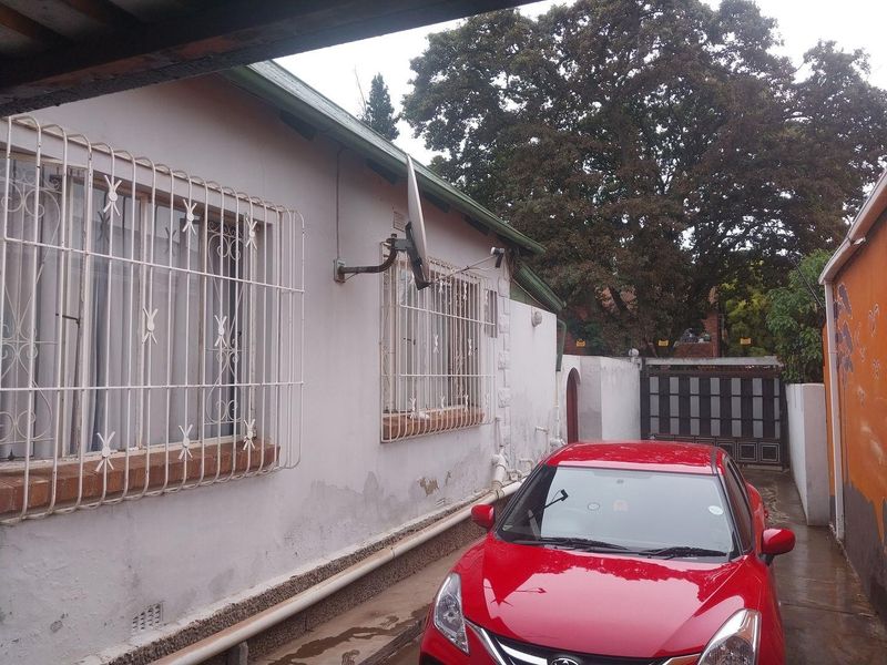 Side exterior view of the property showing a paved driveway, security bars on windows, and boundary walling.